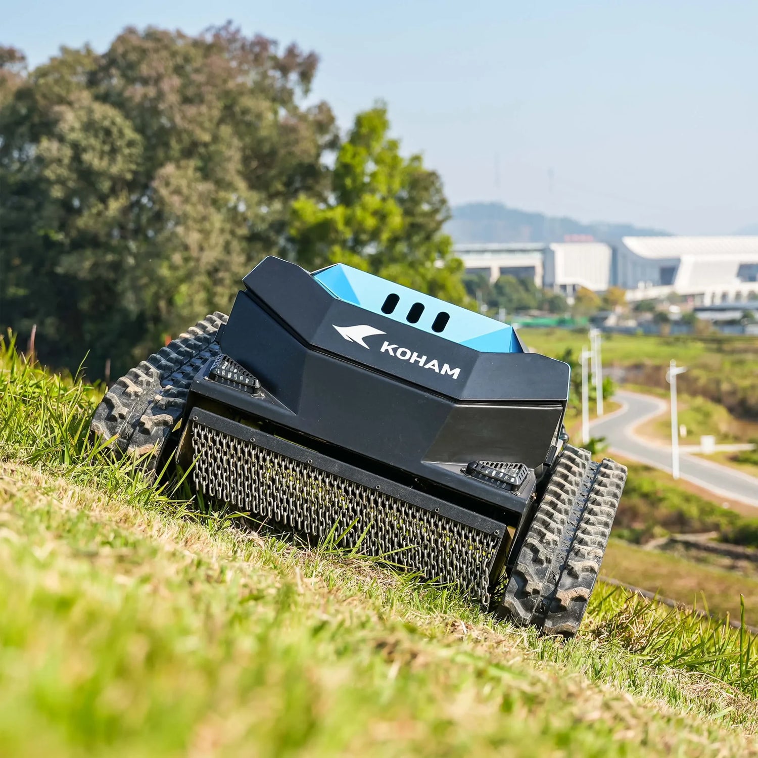 RC lawn mower on grass with trees and buildings in the background
