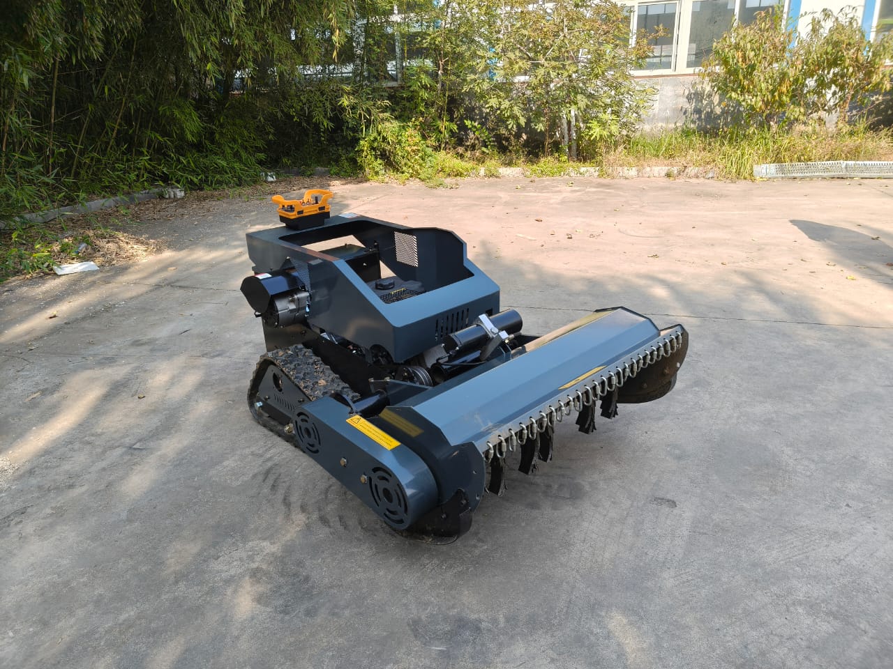 Remote control lawn mower on a concrete surface with greenery in the background