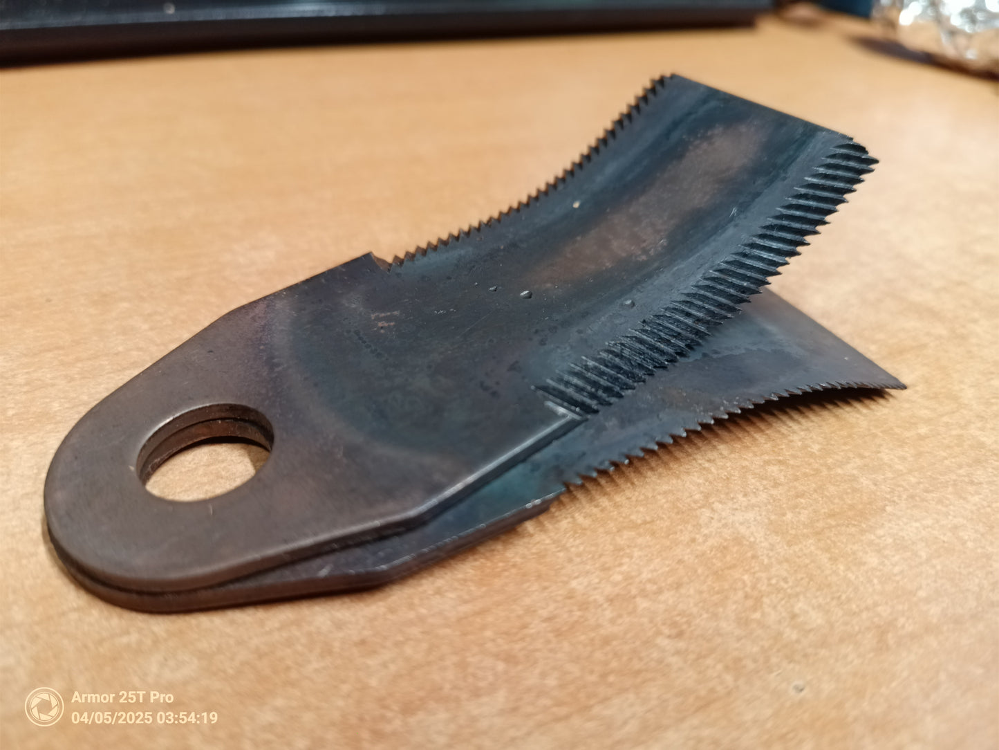 Black metal tool with a comb-like top and hole in the middle on a beige surface.