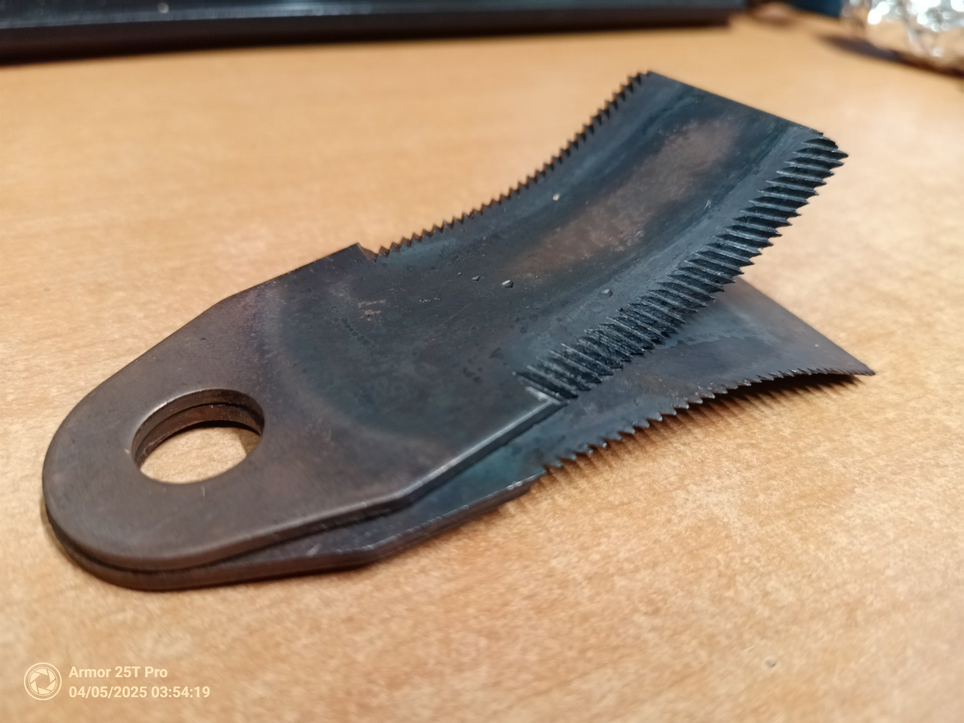 Black metal tool with a comb-like top and hole in the middle on a beige surface.