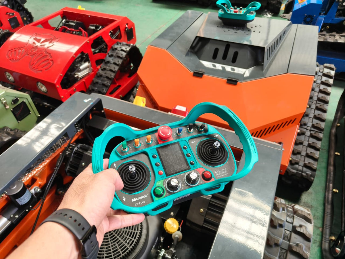 Hand holding a turquoise remote control for the Redback remote control lawn mower, showcasing its features.
