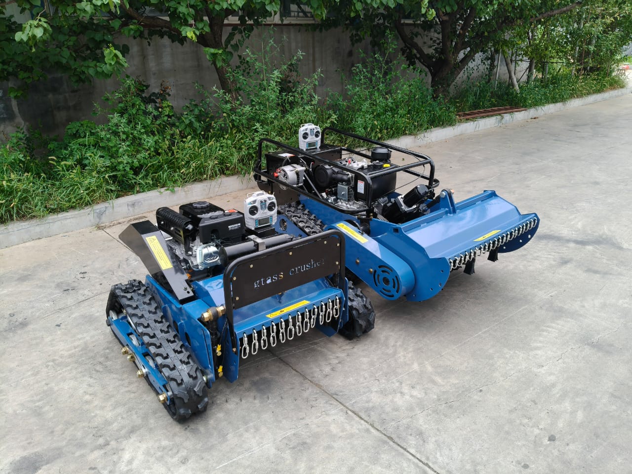 comparison of two remote control lawn mower on a driveway with greenery in the background
