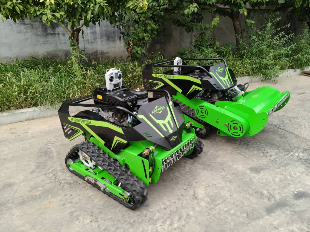 Two green tracked remote control mowers on a concrete surface with greenery in the background