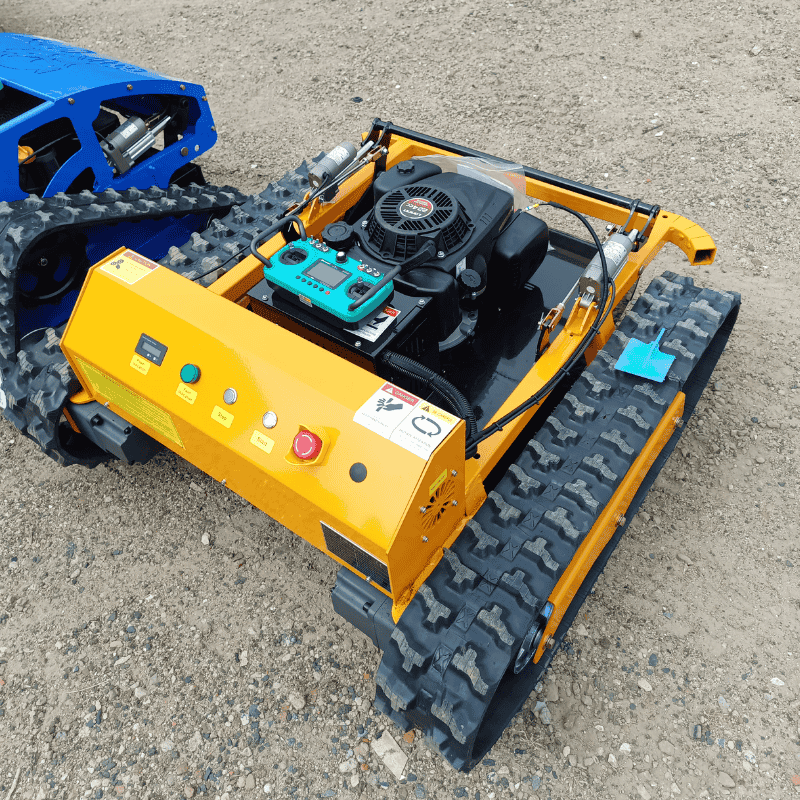 Radio controlled lawn mower remote control with 9HP engine and tracked drive system on gravel surface.